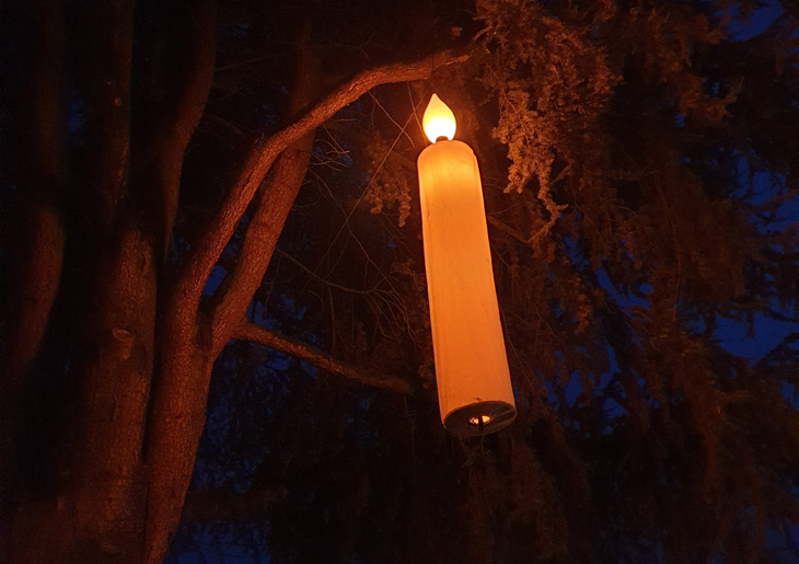 foto van een hele grote (namaak) kaars in boom bij avondlicht